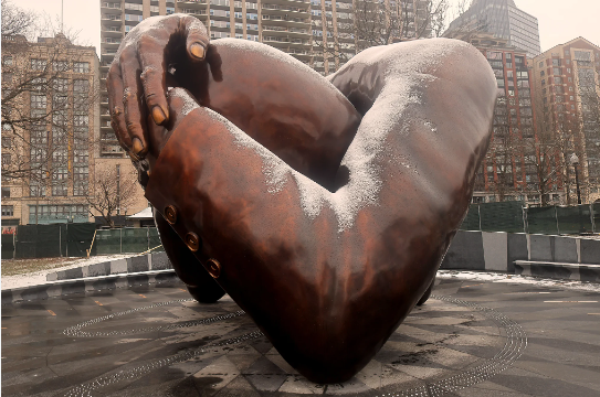 Bronze sculpture of embracing arms in a snowy outdoor setting, symbolizing connection and support.