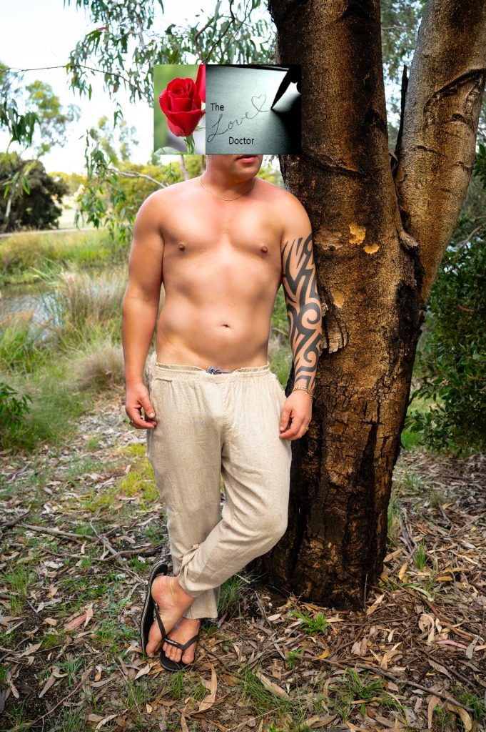 Man in linen pants leans against a tree, a rose overlay obscures his face.