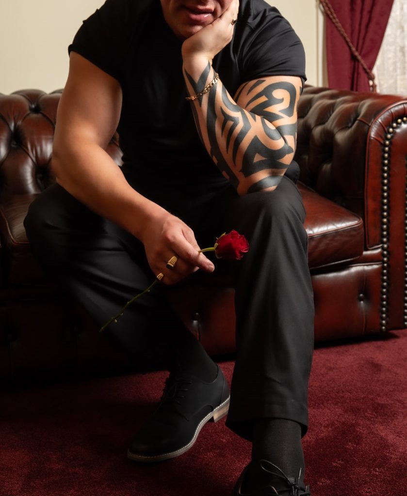 Man with arm tattoo holding a red rose on a leather sofa, February 2025 gallery