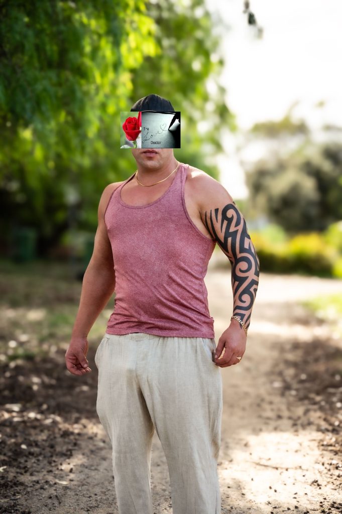 Man with tattoo and rose on face stands in a park path.