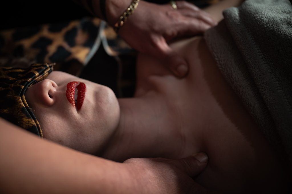 Close-up of a person receiving a chest massage, with red lipstick and a leopard print eye mask.