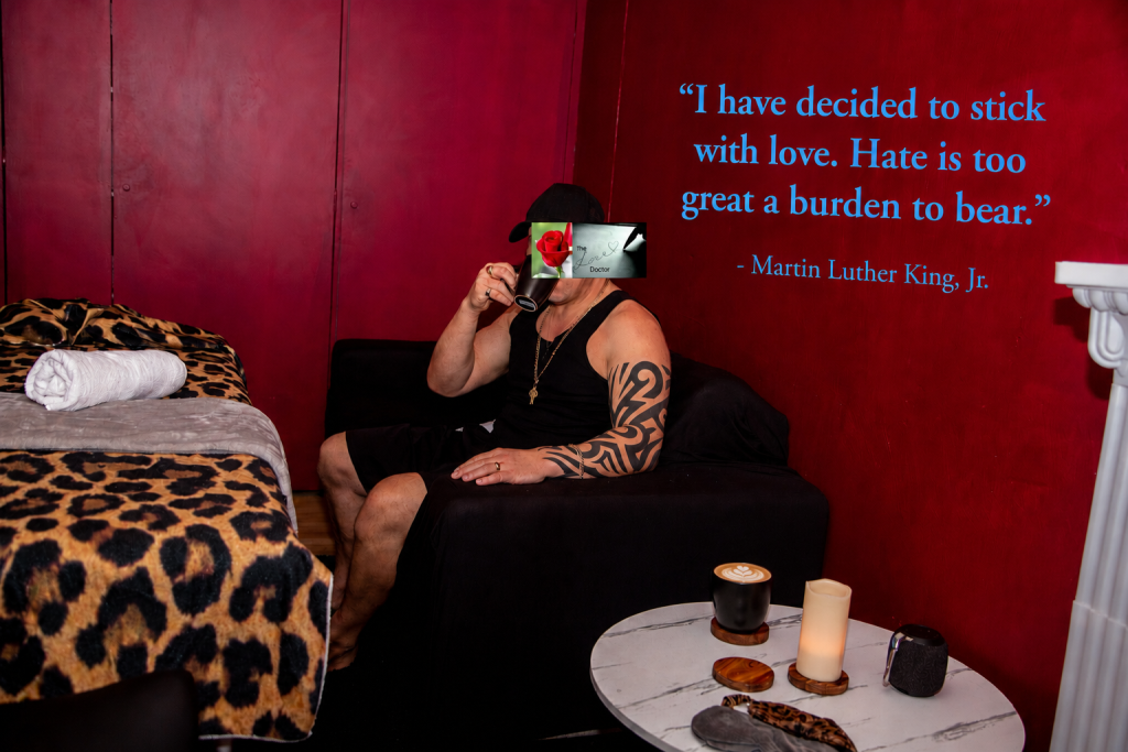 Man in tank top drinks from mug in red room with quote by MLK Jr.