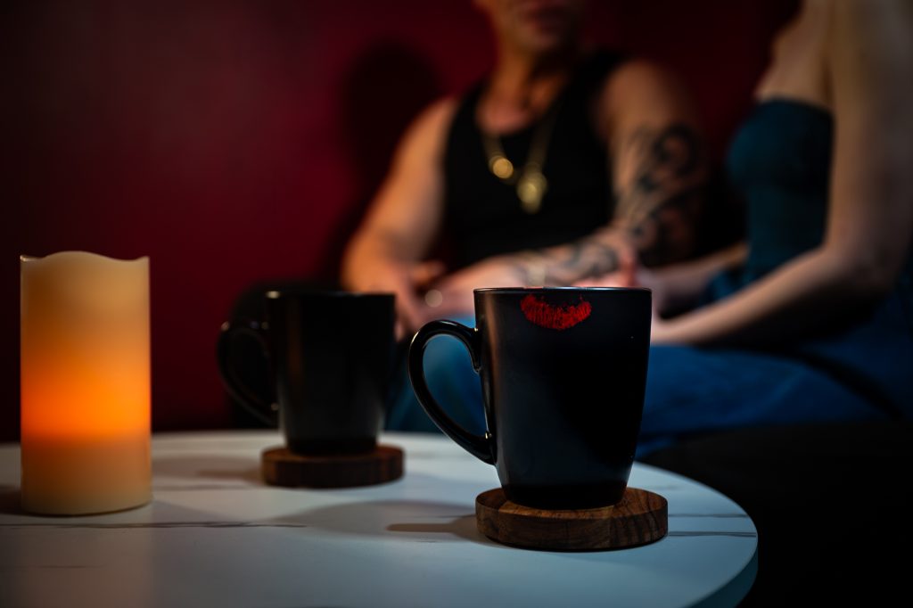 Two mugs with a lipstick kiss mark and a lit candle on a table.