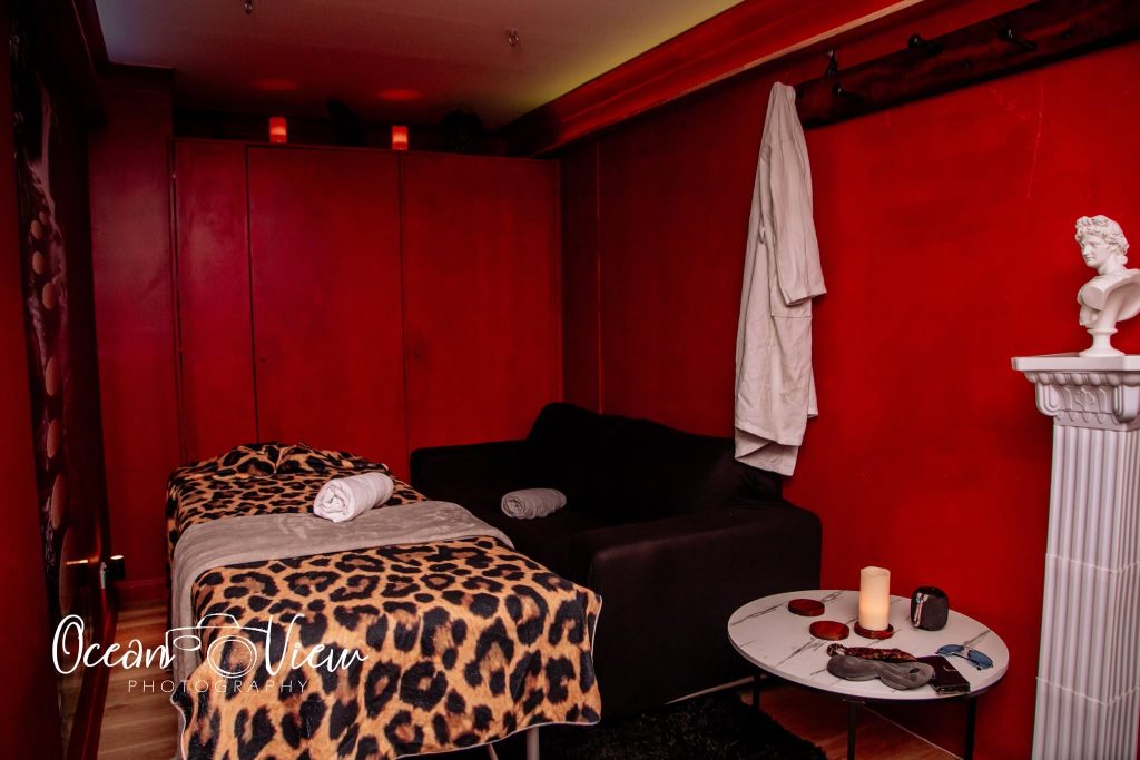Massage studio room with a leopard print massage table, couch, and red walls.