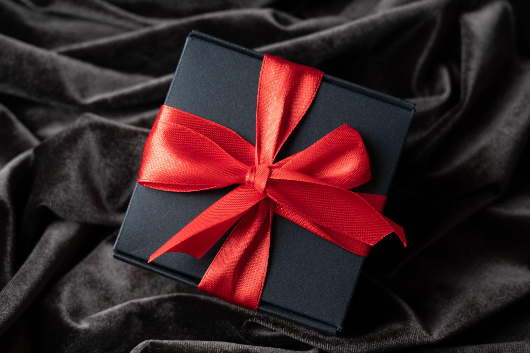 Black gift box with red ribbon on velvet fabric