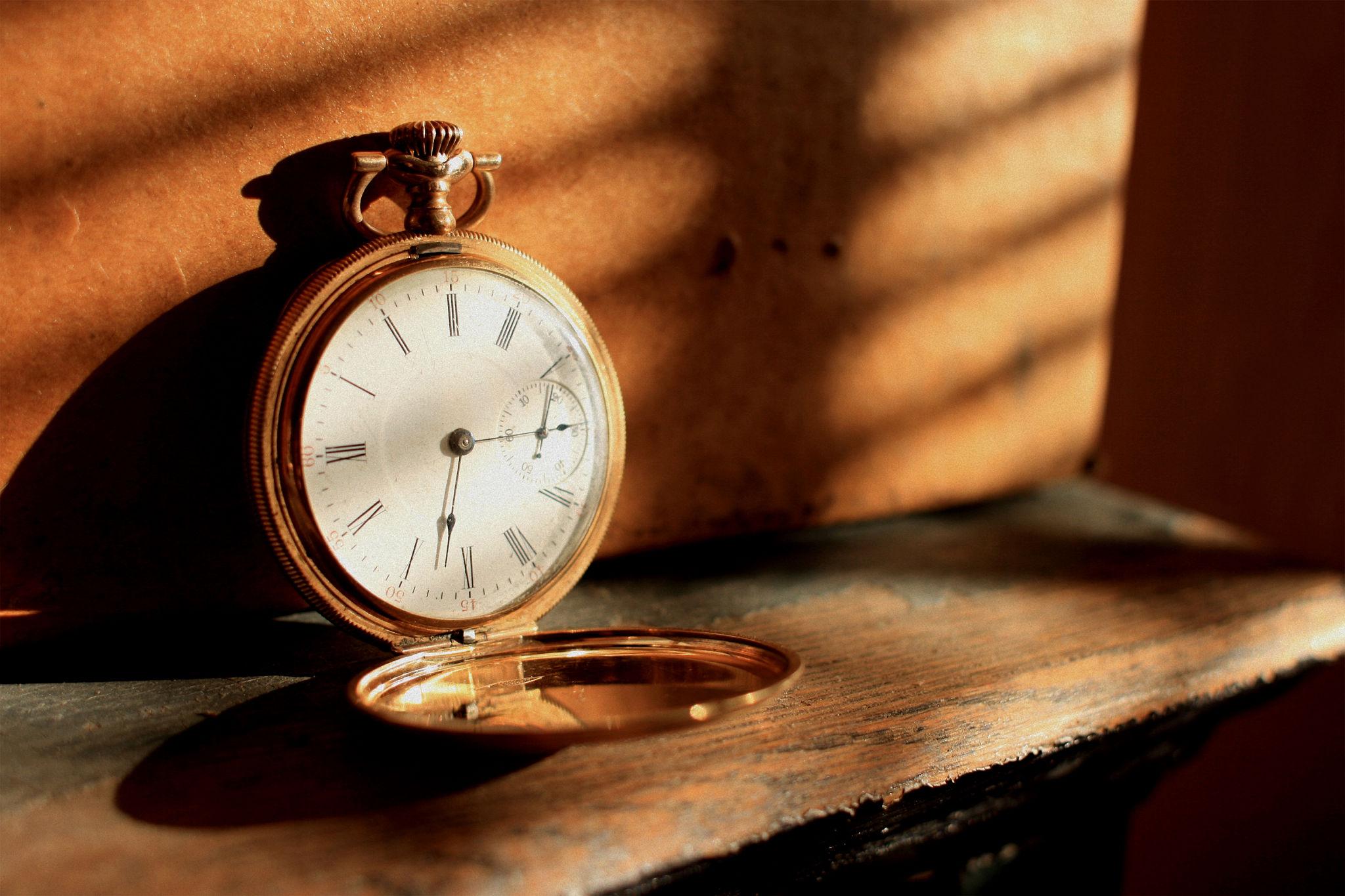 Vintage pocket watch on a wooden surface, bathed in sunlight